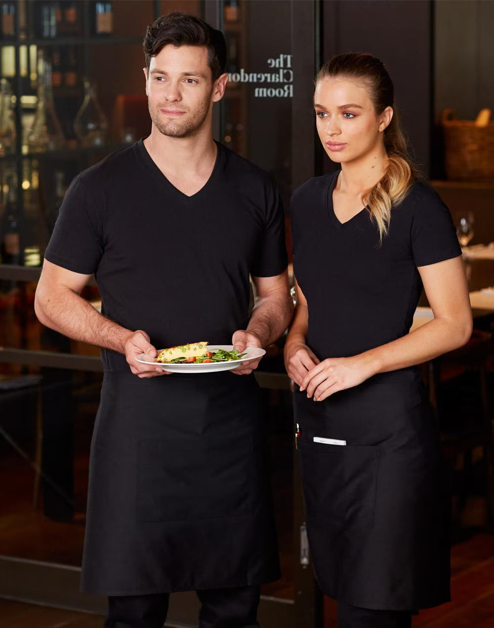 Two servers in black uniforms holding a plate of food in a restaurant setting.